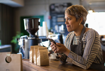 Una persona trabajando en una cafetería, levanta la vista del teléfono móvil y sonríe.