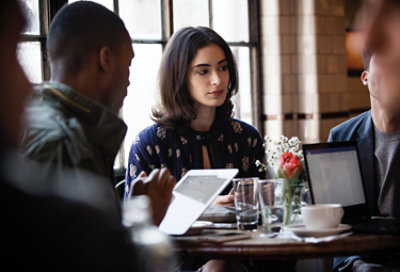 Tres personas sentadas en un restaurante en una reunión de almuerzo. Una de ellas está usando un portátil y otra una tableta.