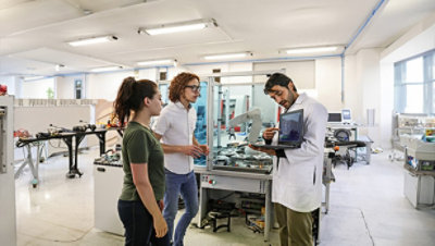 Three people working together on a project in a well-lit, modern laboratory setting. One person is wearing a white shirt