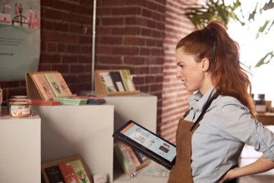 אדם עם שיער ג'ינג'י ארוך אסוף בקוקו, לובש סינר, מחזיק טאבלט 