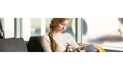 Eine Frau sitzt in einem Flughafen mit einem Tablet und Stift in der Hand.