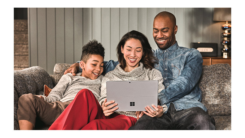 Uma família de três pessoas no sofá de casa assistindo a algo em seu tablet