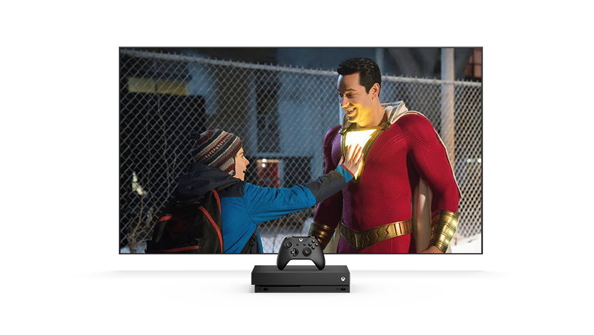Tela de TV mostrando um menino tocando o peito aceso de um homem usando uma fantasia de super-herói