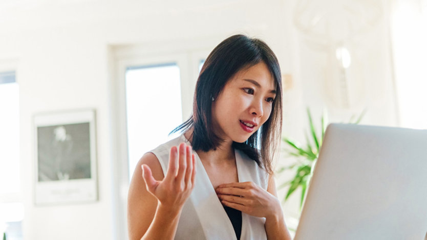 Woman sitting at desk looking at a laptop with a quizzical look.