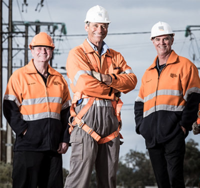 Tri nasmejana zaposlena iz preduzeća SA Power Networks nose zaštitna neonska odela i šlemove.