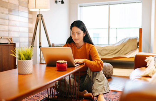 Woman sitting at coffee table on living room floor using Windows 11 laptop