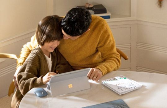A father and daughter sitting at a round table working together on a Windows 10 PC