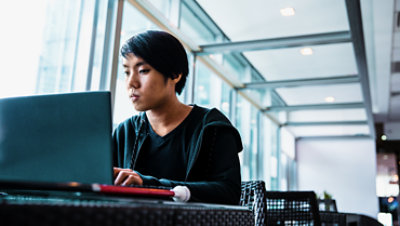 Debra Droz, a woman who is hard of hearing, wears headphones and types on a laptop