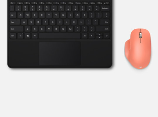 Şeftali Rengi Microsoft Bluetooth® Ergonomic Mouse, bir tuş takımının yanında masanın üzerinde duruyor