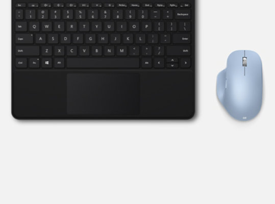 Pastel Mavi Microsoft Bluetooth® Ergonomic Mouse, bir tuş takımının yanında masanın üzerinde duruyor