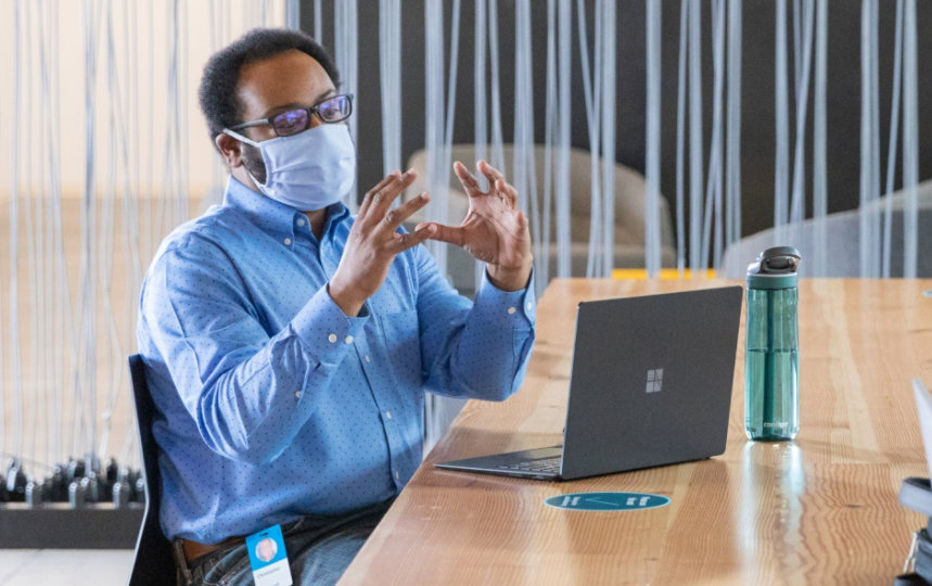 Two businesspeople at a table with laptop devices, socially distanced, wearing masks.