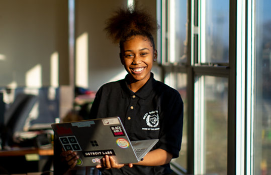 A student smiling and holding a laptop in a classroom