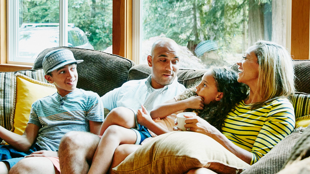  Family of four sits together on a couch at home