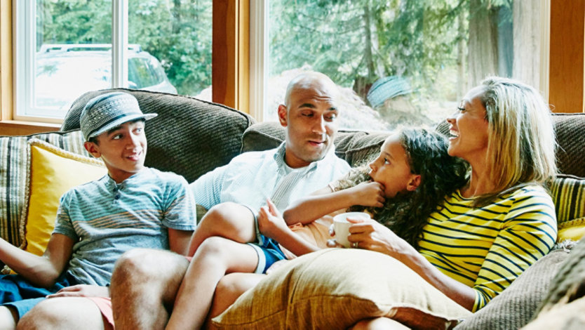 Photo credit: Thomas Barwick/DigitalVision/Getty Images. Family of four sits together on a couch at home.