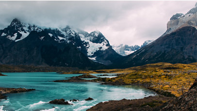 A blue lake in front of mountains partially covered by clouds