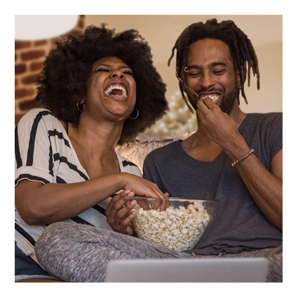Laughing man and woman eat popcorn together on the couch at home while watching a video conference on laptop computer