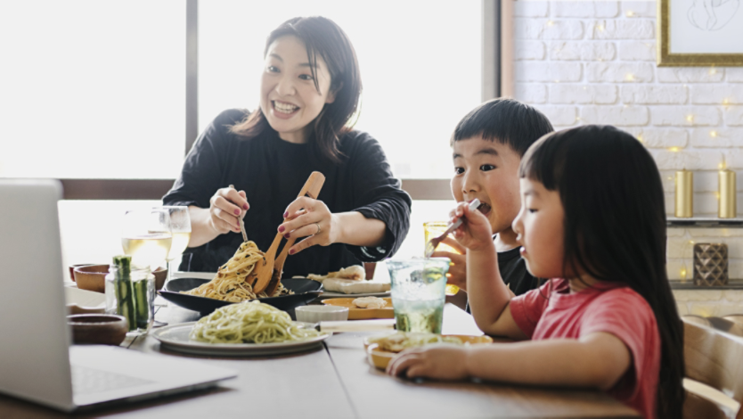 Mother and two children eat a meal together in kitchen while conducting video call on a Windows laptop