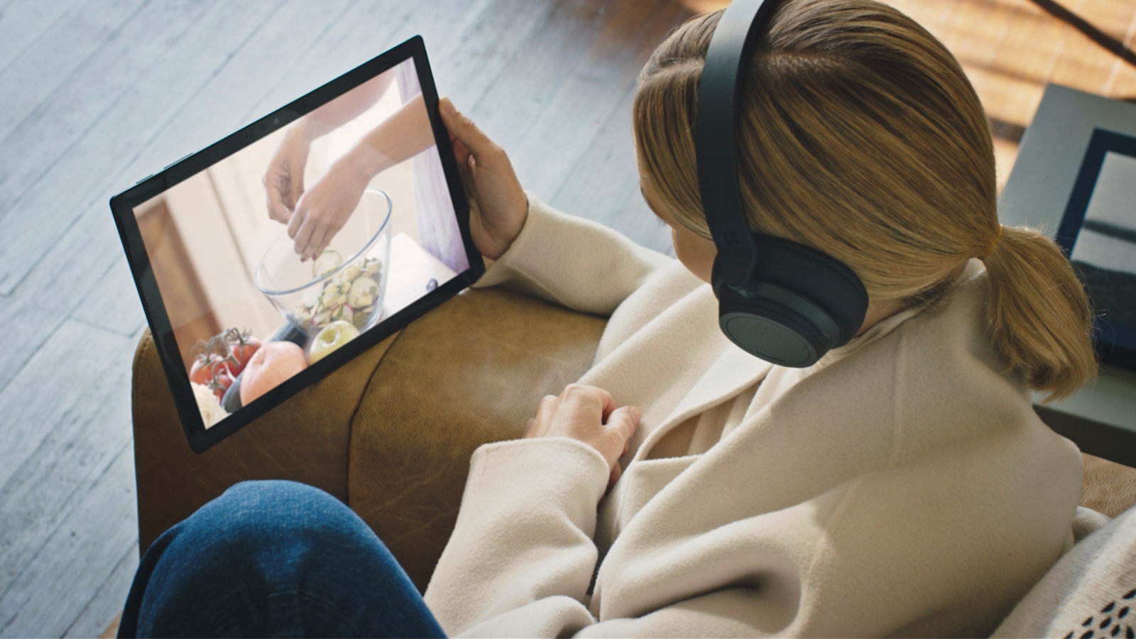Woman holding a Surface Pro 7, watching a cooking video with black Surface Headphones on
