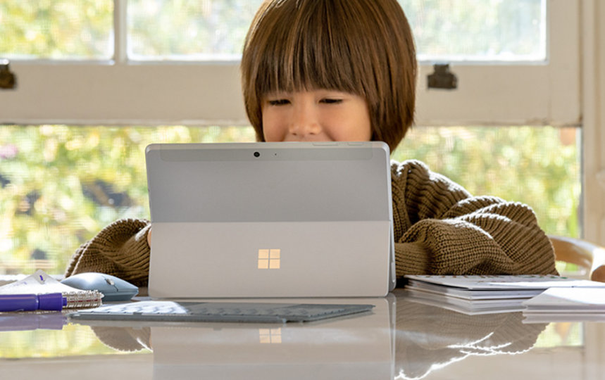 自宅でアイス ブルーの Surface タイプ カバーが装着された Surface Go 2 を Surface ペンで使う幼い子供