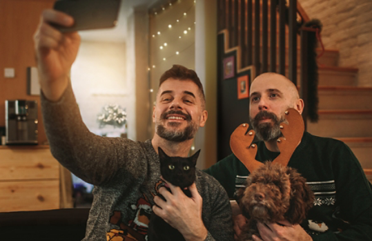 Two men photograph themselves at home while holding a cat and a dog