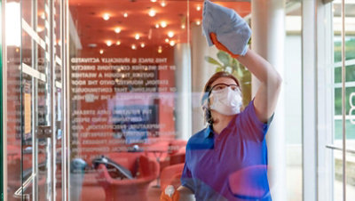 En kvinde iført en maske desinficerer en glasdør.