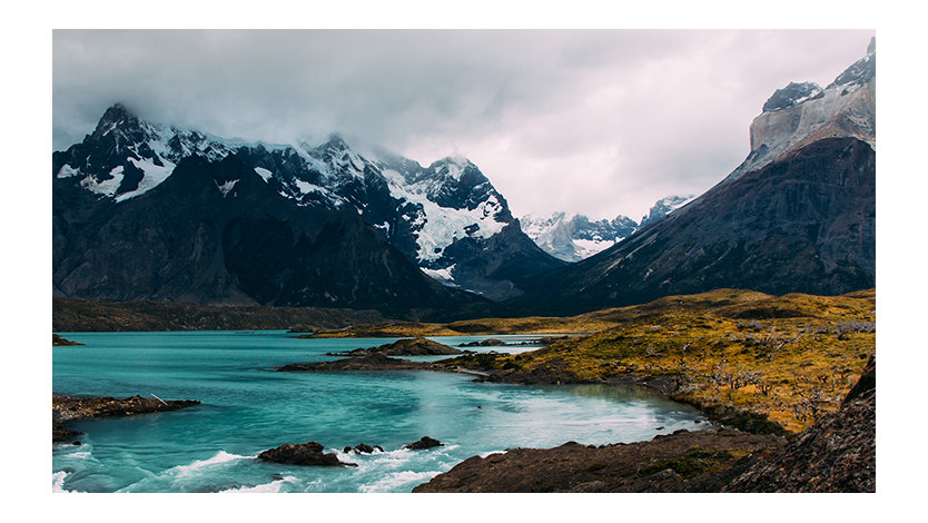 A blue lake in front of mountains partially covered by clouds.