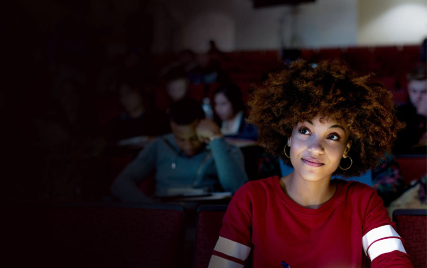 Close up of female college student sitting in university lecture hall. She is smiling and looking ahead. 