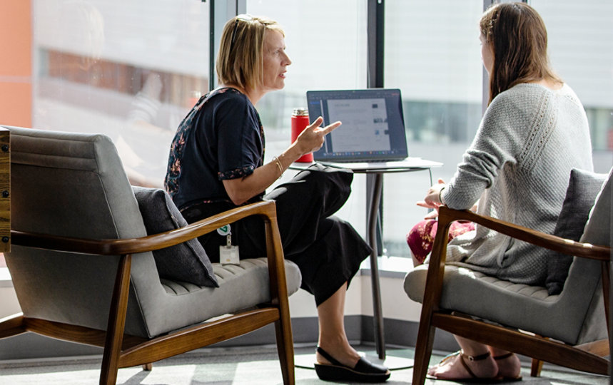  Two female tech workers collaborate in a common office space.