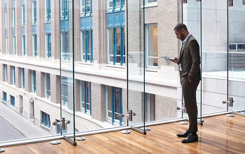 A male business professional in a large foyer is on a mobile device.
