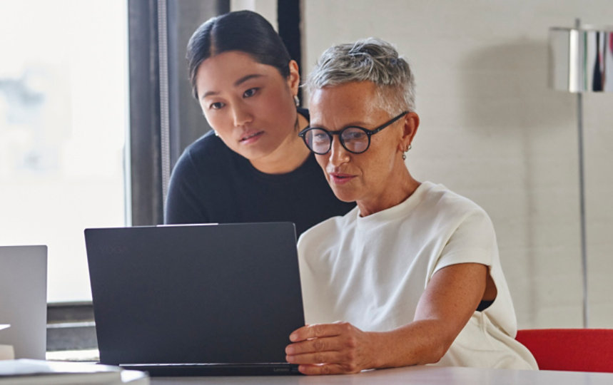 Two women at a desk with laptops open in conversation.