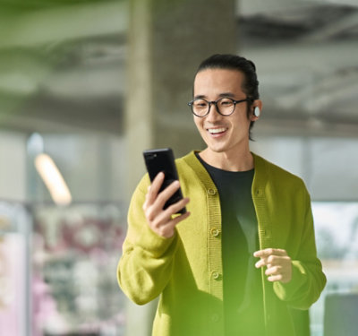 Osoba koja se smeje, nosi slušalice u ušima i koristi mobilni telefon