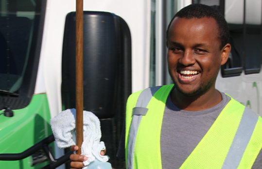 Smiling man in a safety vest, holding cleaning supplies