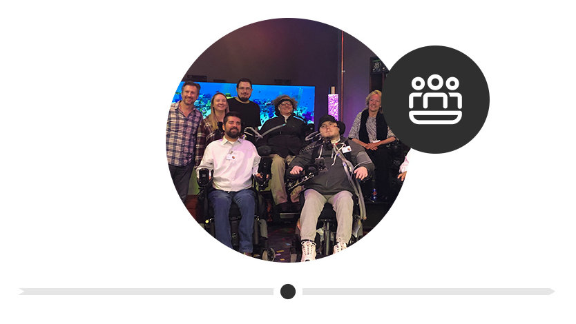 Seven people posing for a picture at the original Inclusive Design Lab, four of them are men who are tetraplegics in wheelchairs.