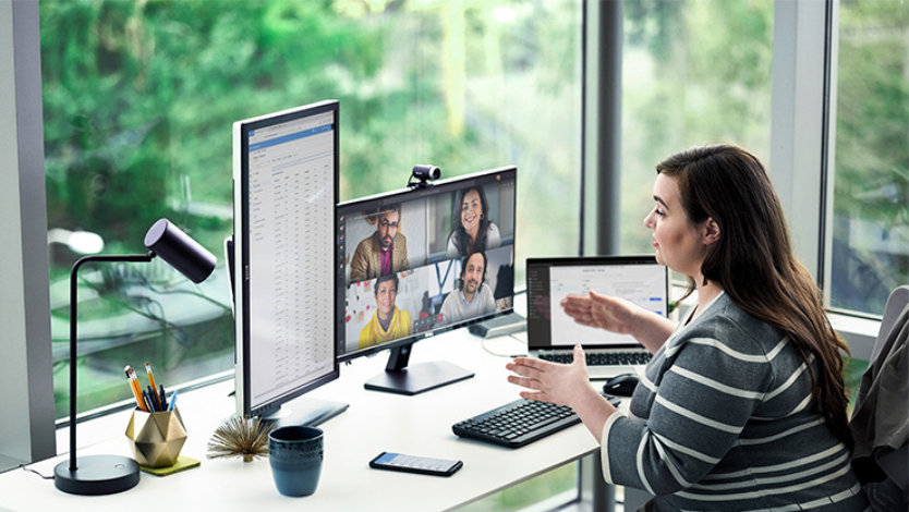 여러 장치를 사용하여 책상에서 작업하면서 Microsoft Teams로 전화 회의를 실행 중인 여성.