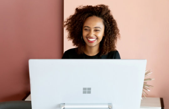 Smiling woman sitting behind a Microsoft-branded computer.