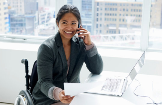 Smiling woman working in office while sitting in wheelchair.