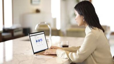 Henkilö istuu keittiösaarekkeella ja käyttää kannettavaa tietokonetta.