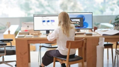 Henkilö istuu pöydän ääressä työskentelemässä kahdella näytöllä.