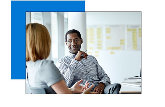 A man sitting in a chair looking at his coworker and listening to what she is saying