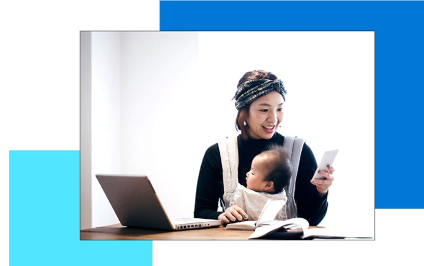 A woman working at a table while holding her baby in a baby carrier 