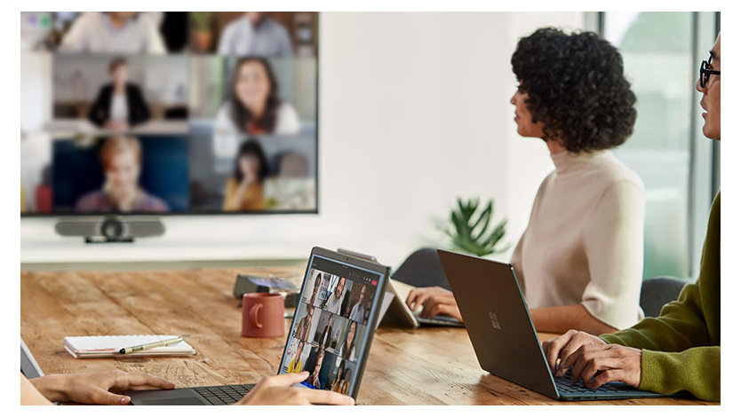 Remote attendees participating in a Microsoft Teams meeting while the front of room screen is displaying Gallery View and a woman has joined on her laptop.