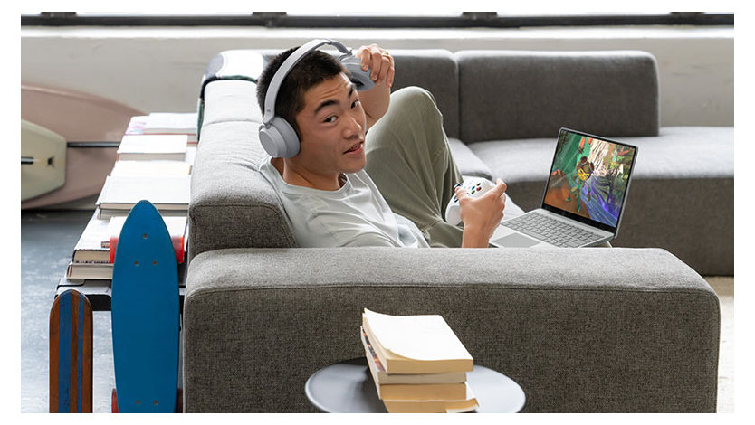 A man wearing headphones relaxing on a couch playing an Xbox game