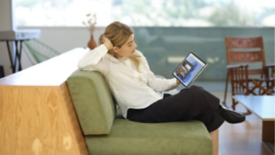 Osoba leżąca na kanapie patrząca na obraz wyświetlany na tablecie.