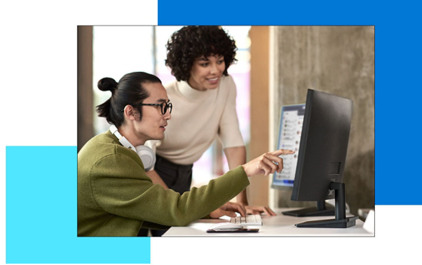 A woman leaning on the desk of her coworker who is pointing at one of his computer monitors