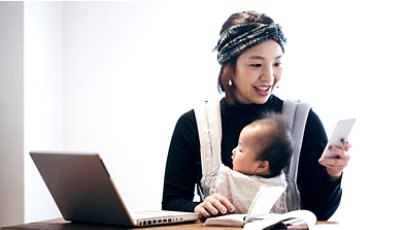 A woman working at a table while holding her child in a front facing baby carrier