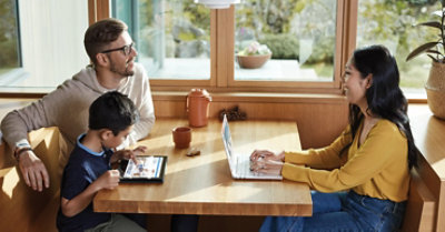 Roditelji i dete za stolom. Jedan roditelj ima laptop, a dete ima tablet uređaj