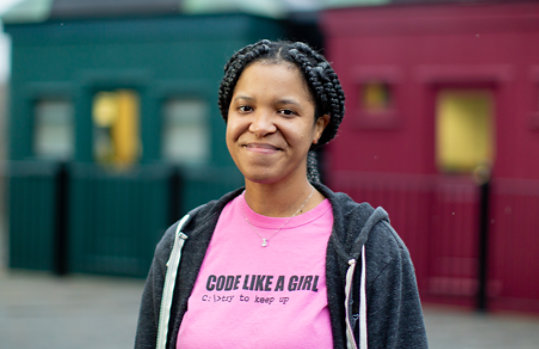 Brandy Foster stands outside, smiling, wearing a “Code like a girl” shirt