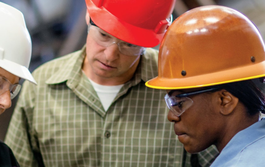 Three manufacturing workers looking at a handheld device.