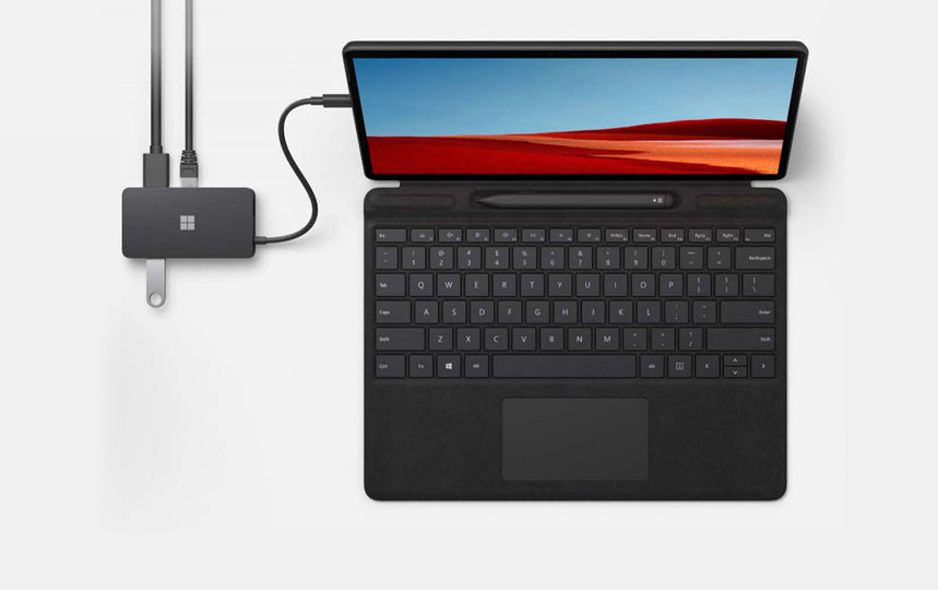 A Microsoft USB-C® Travel Hub sits on a desk, plugged into a Surface device.