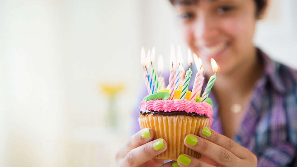 A smiling woman holding a cupcake with colorful birthday candles